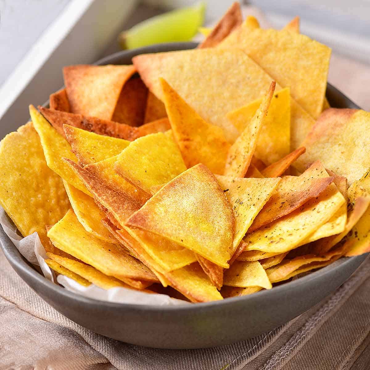 Crispy air fried corn tortilla chips in a gray bowl with a lime wedge ready to be served.