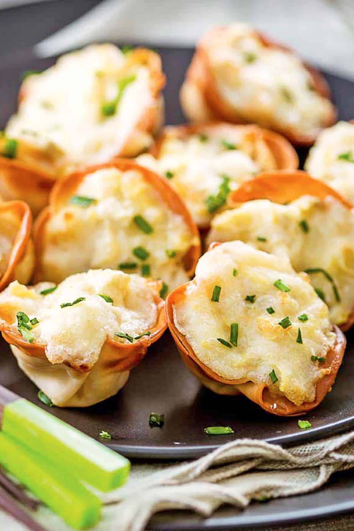 A dozen artichoke wonton wrappers appetizers on a black plate.