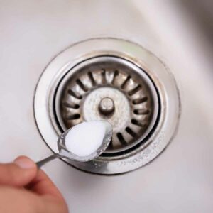 Pouring baking soda down a clogged sink with a spoon.