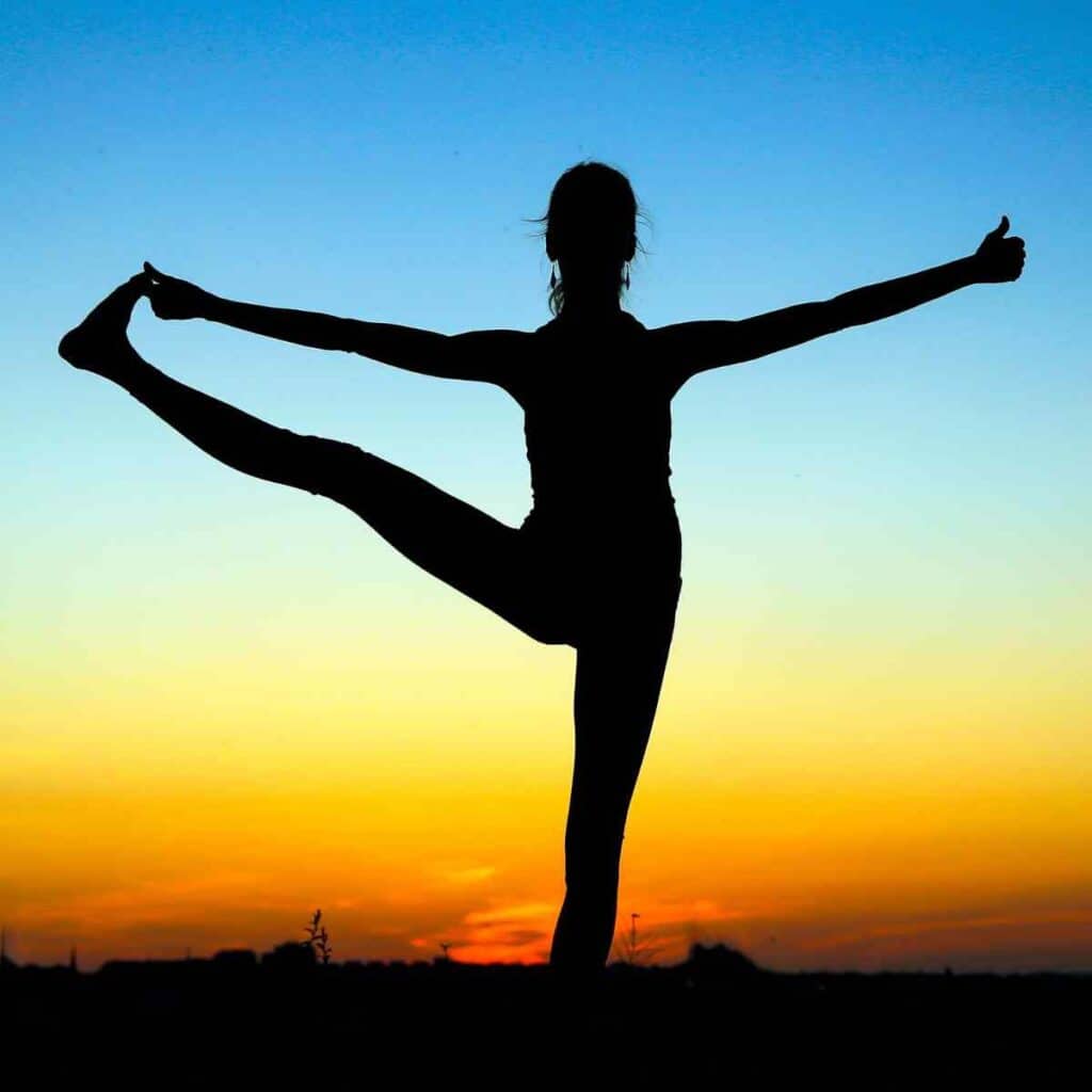 A woman balancing while doing yoga on the beach.