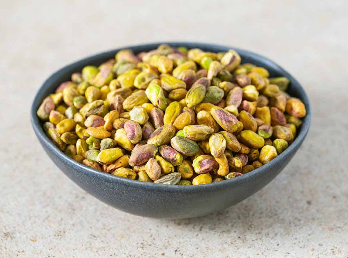 A ceramic bowl filled with shelled roasted pistachio nuts.