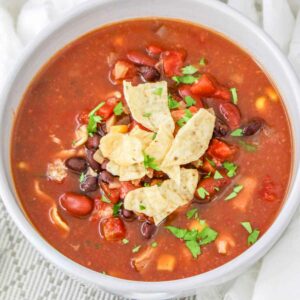 A white bowl filled with southwest chipotle chicken chili topped with tortilla chips and chopped cilantro.