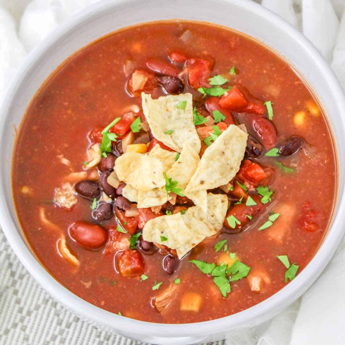 A white bowl filled with southwest chipotle chicken chili topped with tortilla chips and chopped cilantro.