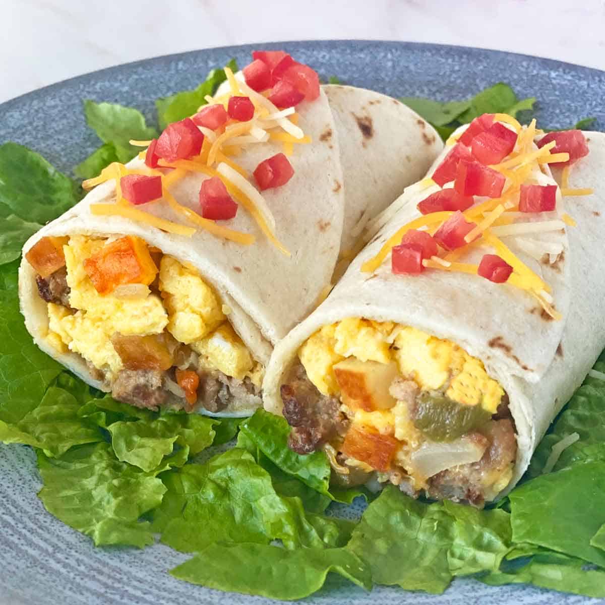 A breakfast burrito cut in half and garnished with chopped tomatoes and cheese.