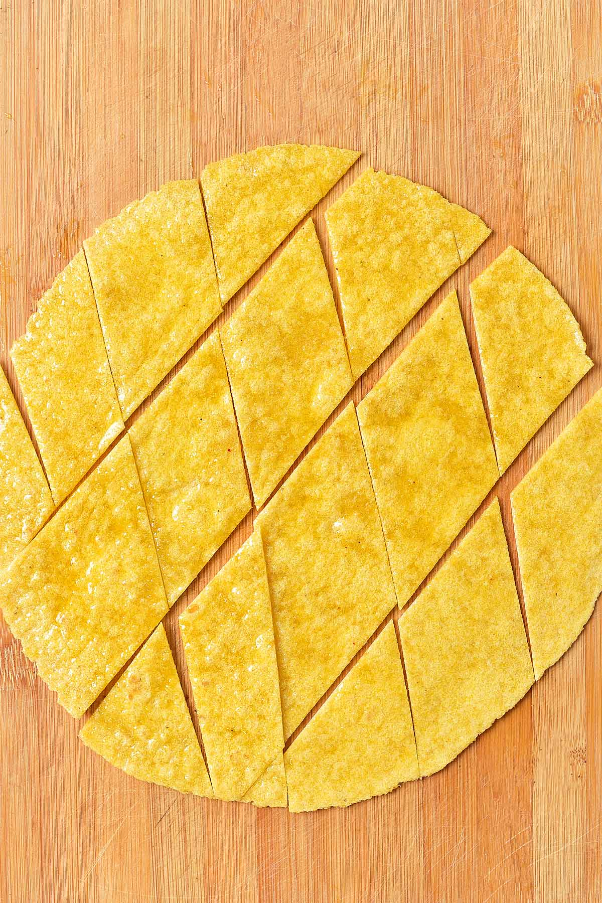 A corn tortilla cut into triangles on a wooden cutting board.