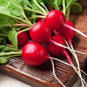 Six radishes grown from seed, with leaves and roots on a cutting board.