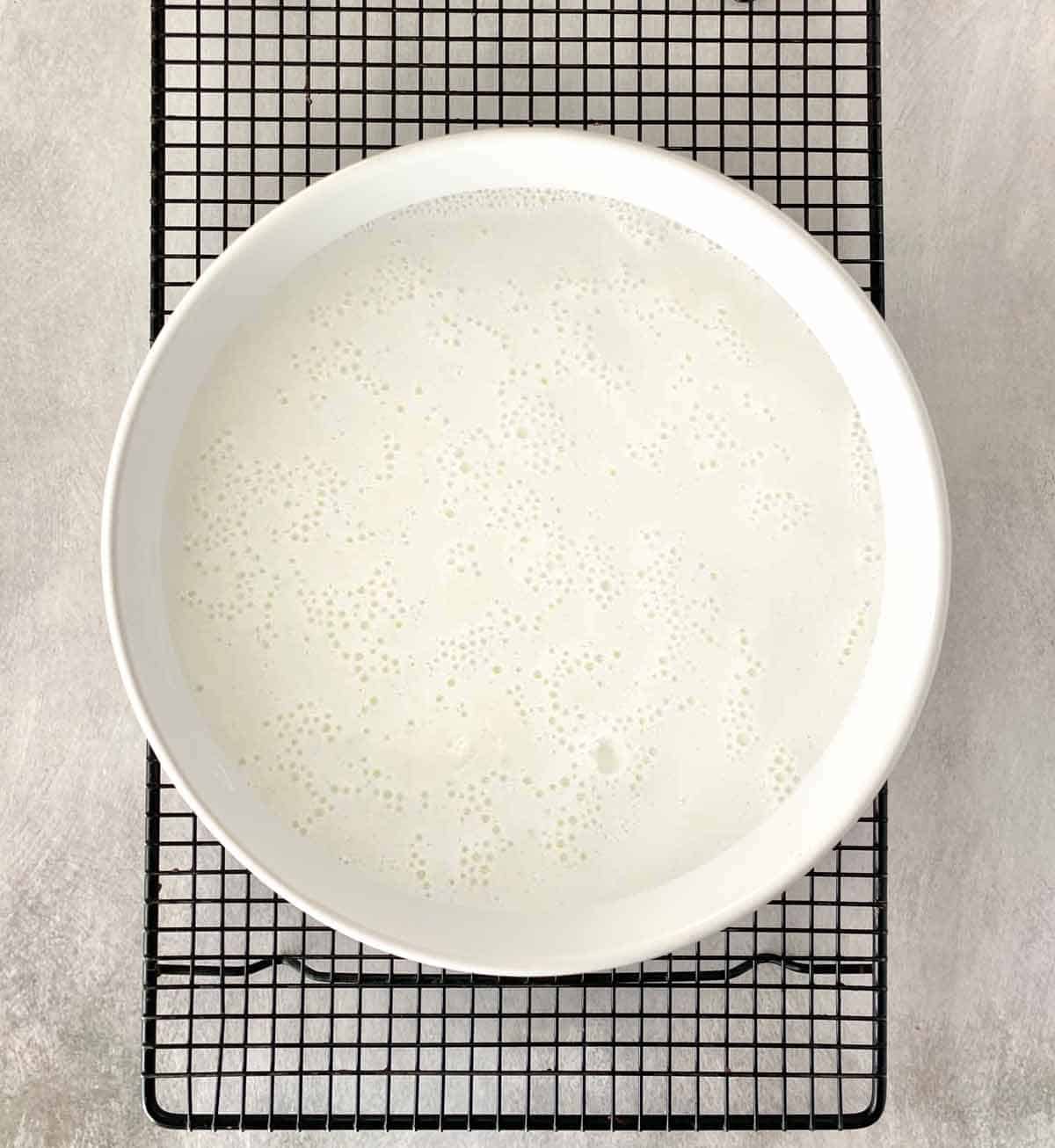 A dish of hot milk resting on a cooling rack.