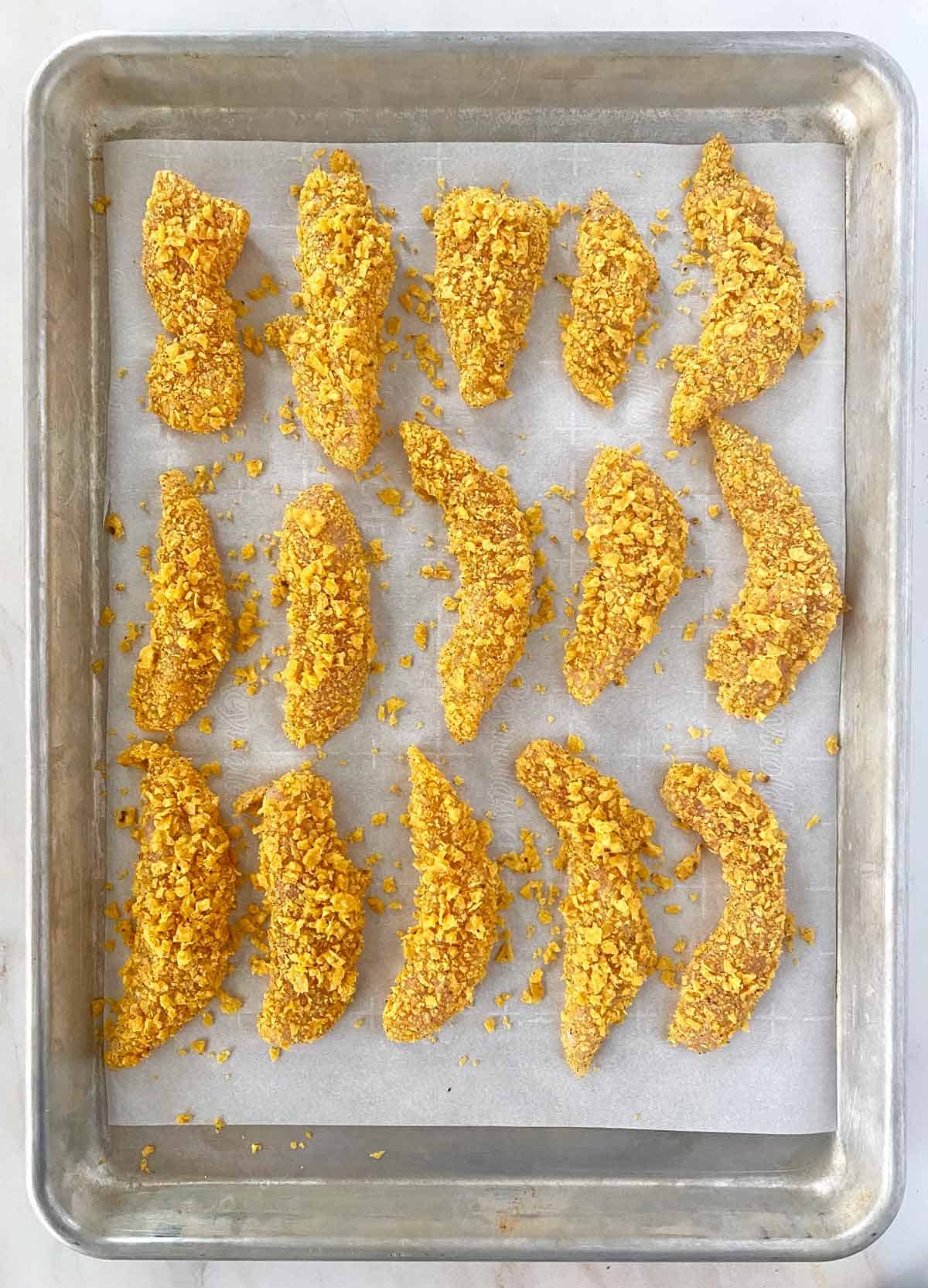 Overhead shot of cool ranch chicken tenders on a baking sheet before being baked. 