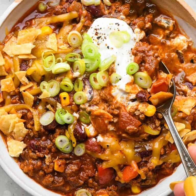 A bowl of chili topped with cheese, sour cream and green onions.