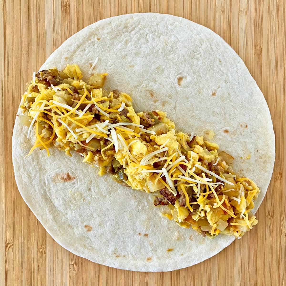 Breakfast burrito filling spooned across a flour tortilla ready to be rolled.