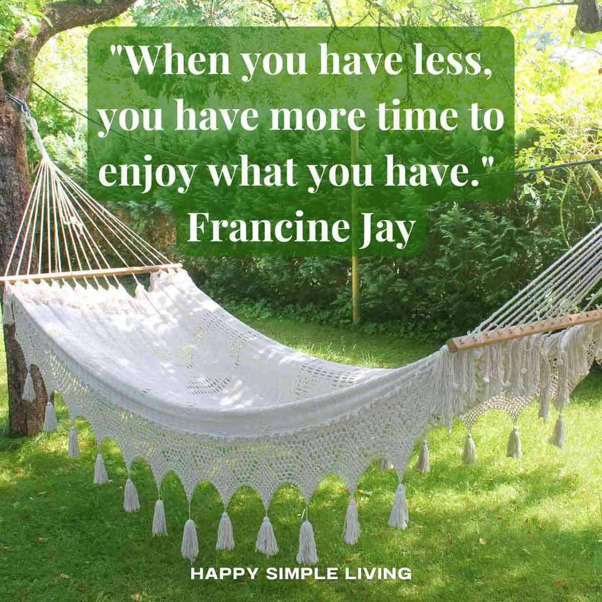 A fringed hammock hanging between two trees in a back yard.