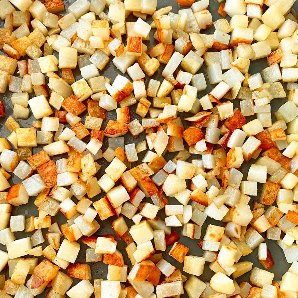 Cubed potatoes frying in a skillet.