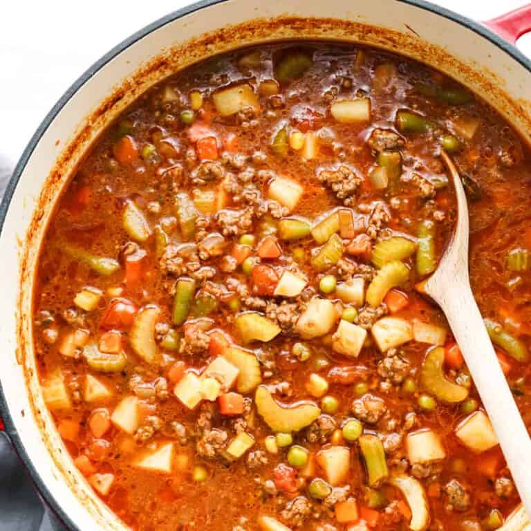 Vegetable soup in a stock pot with a wooden spoon.