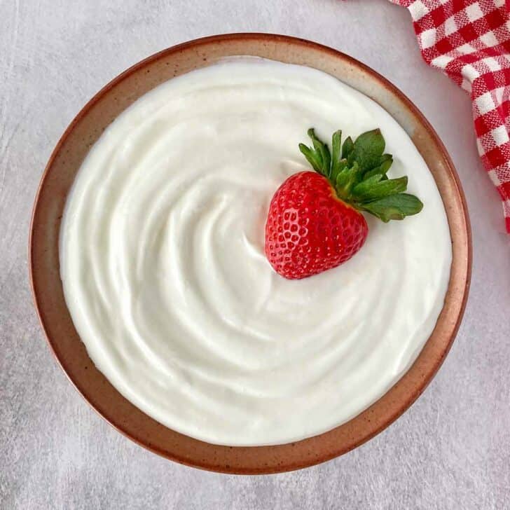 A ceramic bowl filled with Greek yogurt and garnished with a fresh strawberry.