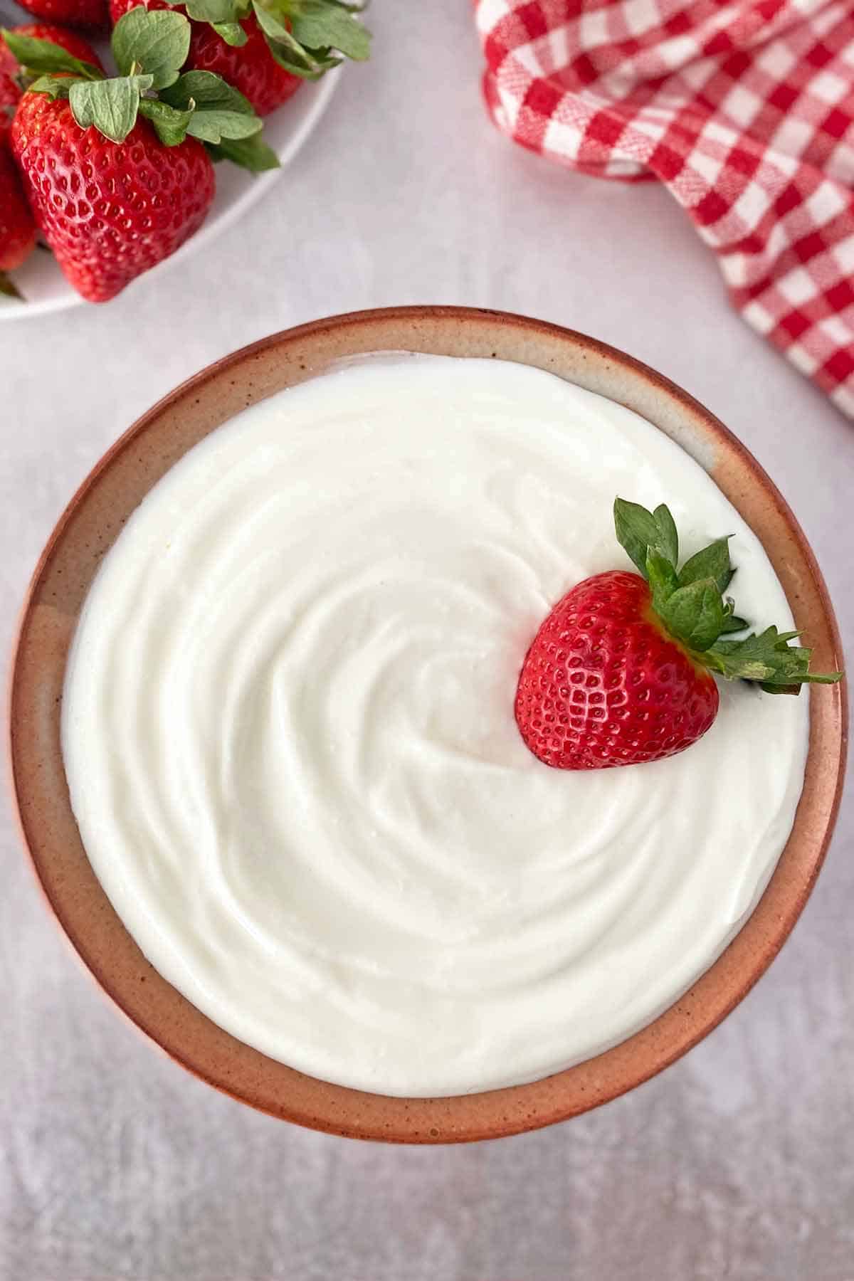 A ceramic bowl of Greek yogurt topped with a strawberry.