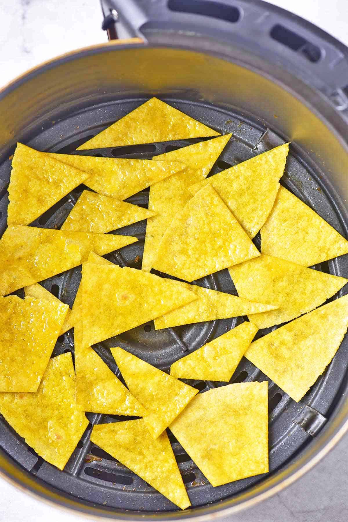 Cut corn tortilla pieces in the basket of an air fryer to make homemade chips.