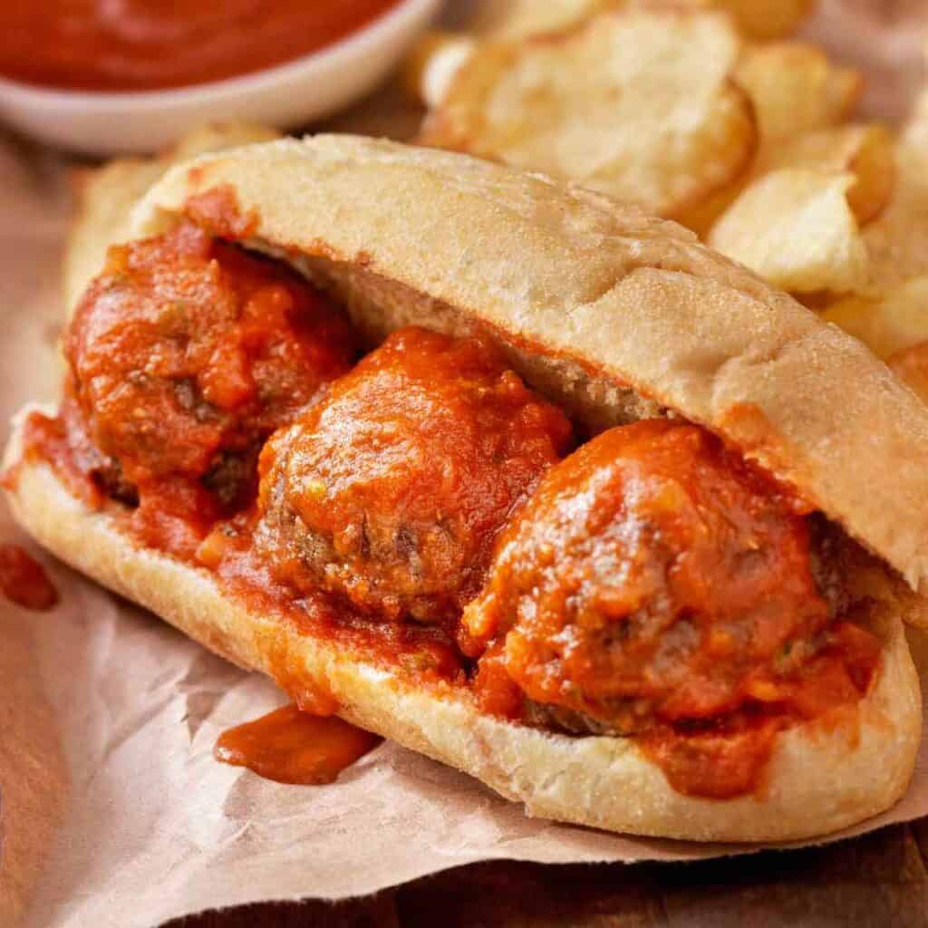 Three meatballs on a hoagie roll with marinara sauce to make a meatball sandwich.