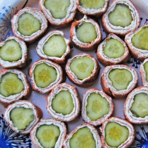 A plate with two dozen pastrami wrapped pickle appetizers.