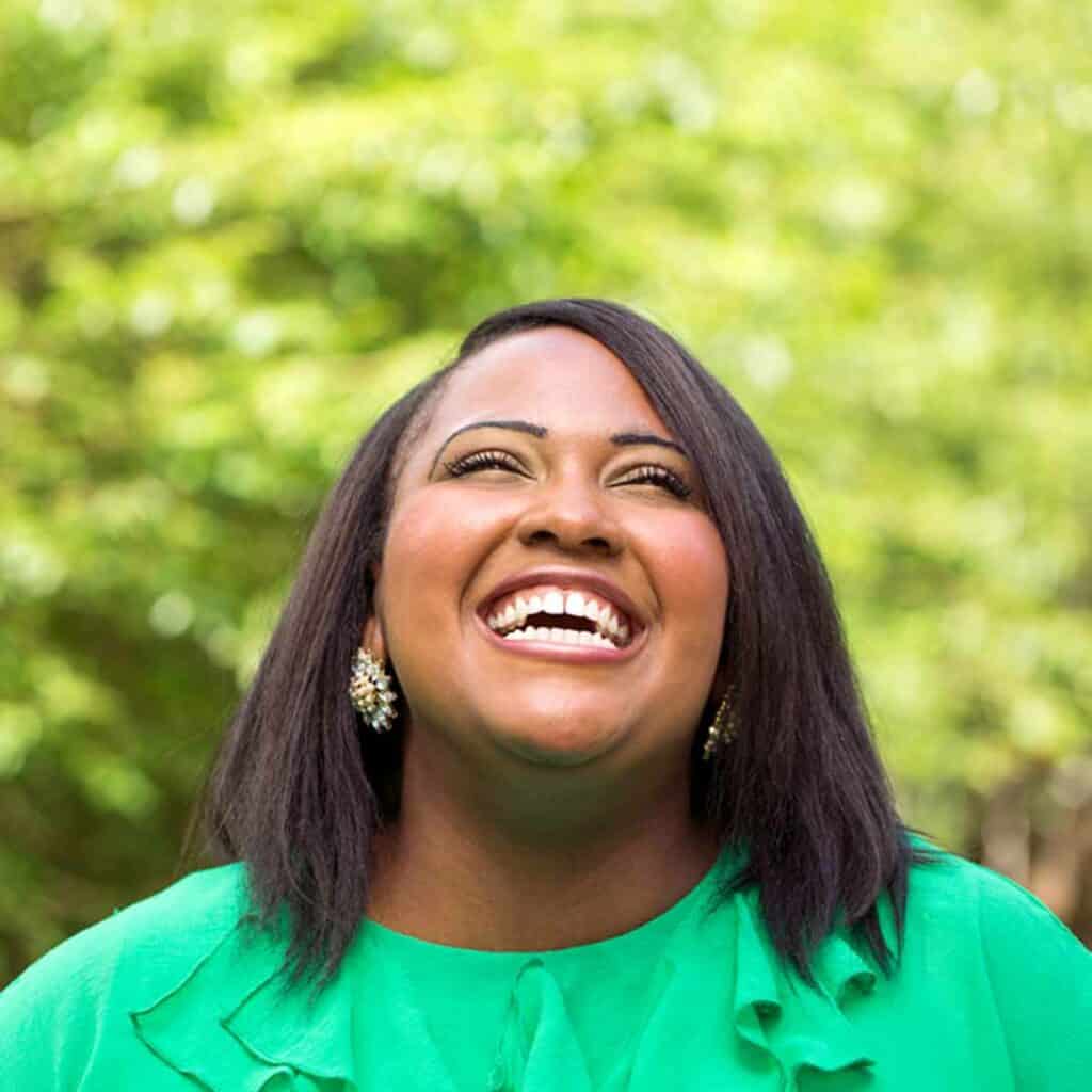 A woman in a green shirt smiling and looking up at the sky.