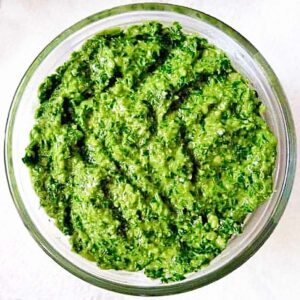 A glass bowl filled with bright green pistachio pesto sauce.