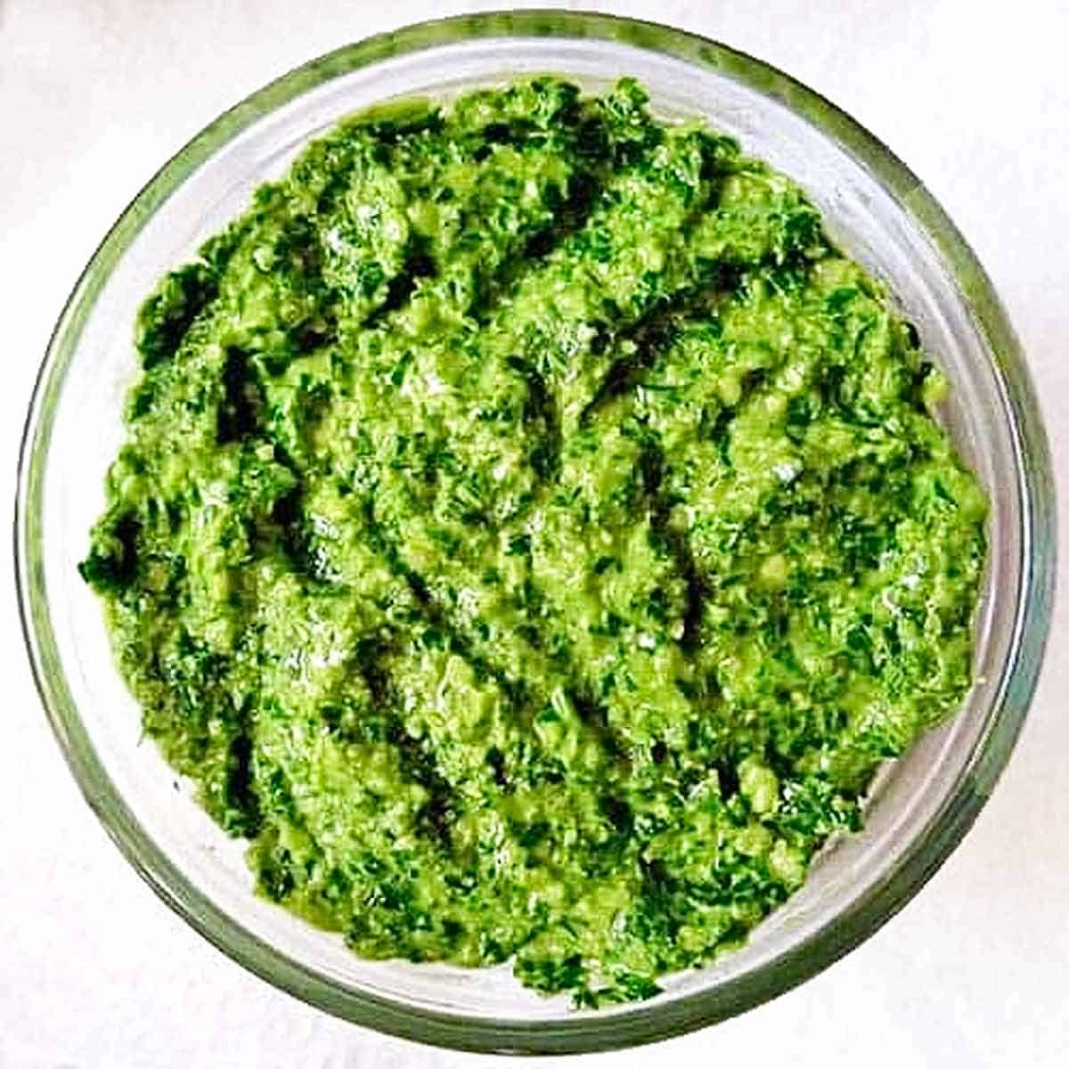 A glass bowl filled with bright green pistachio pesto sauce.