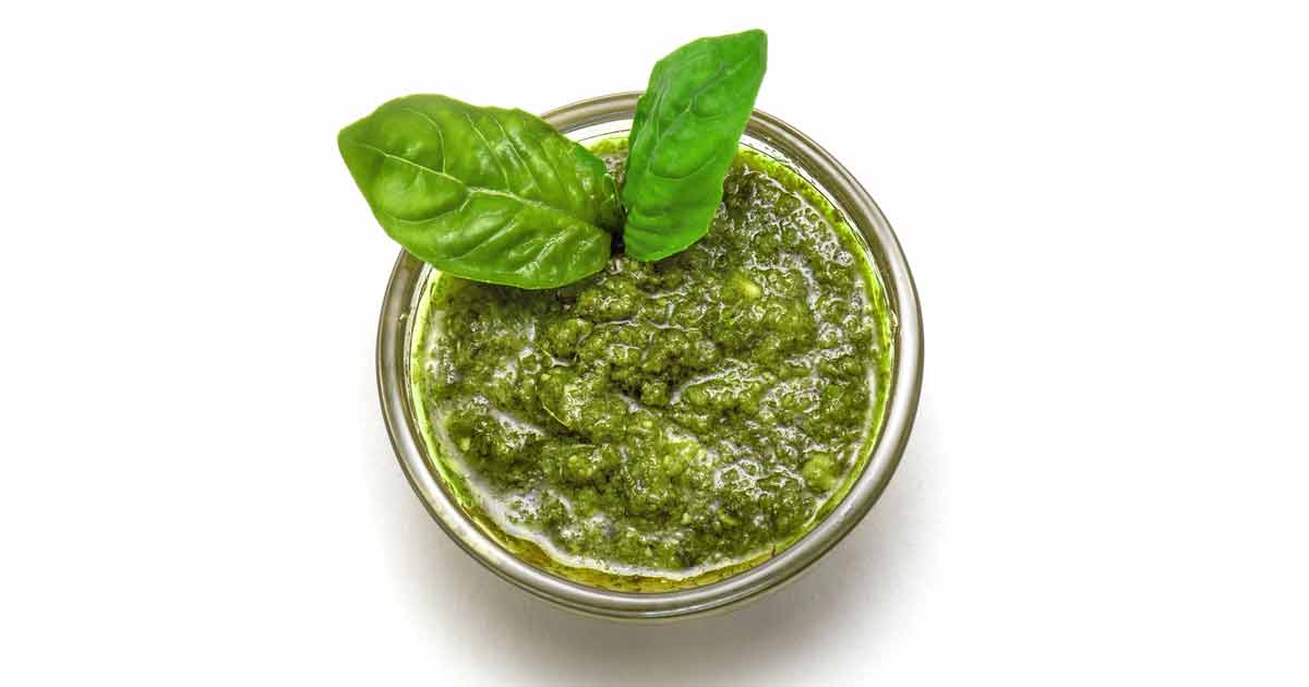 A glass bowl filled with pistachio pesto sauce and garnished with two fresh basil leaves.