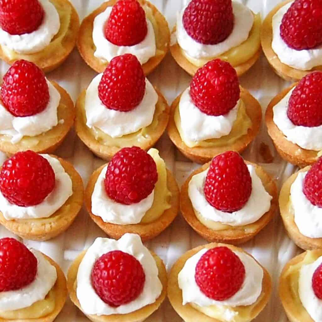 16 mini raspberry custard tarts on a serving dish.