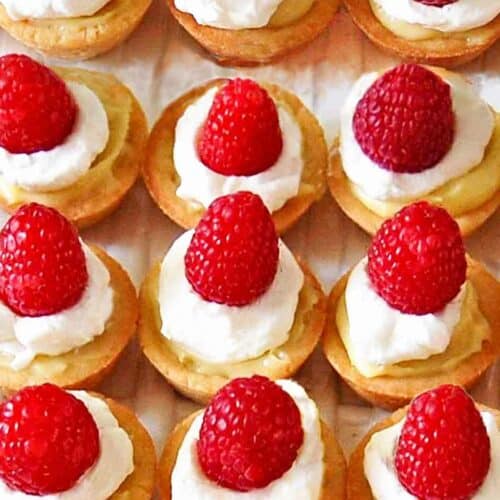 Mini raspberry custard tarts lined up on a serving platter.