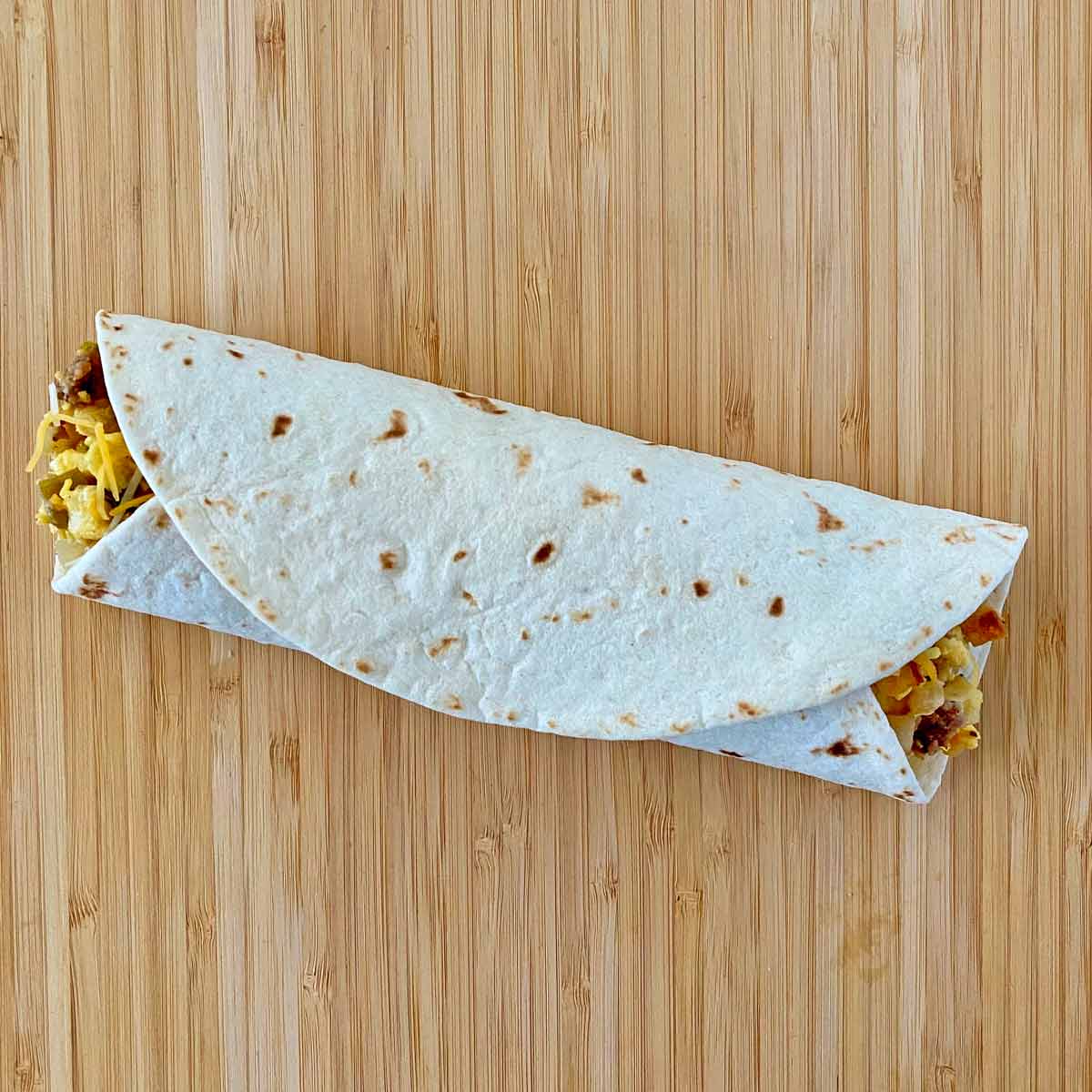 A freshly made breakfast burrito rolled on a cutting board.