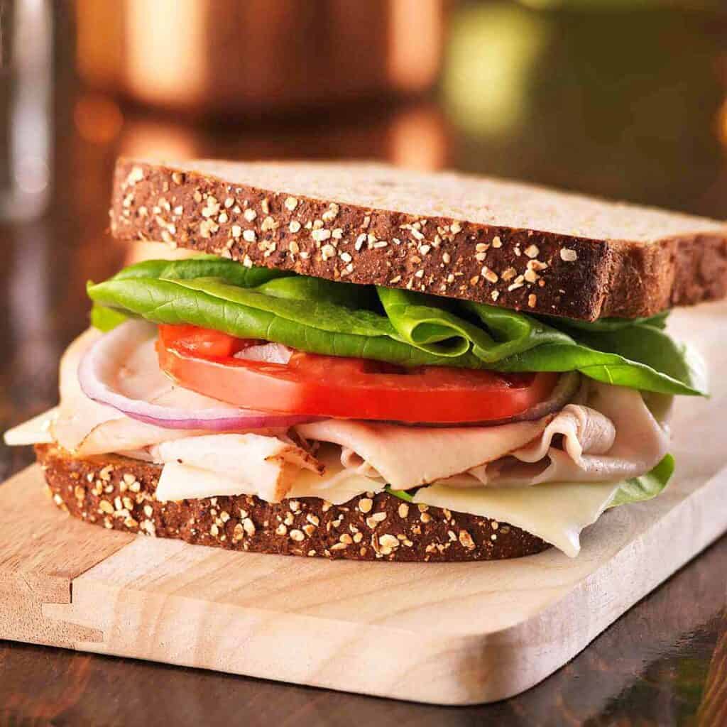 A turkey sandwich on a wooden cutting board.