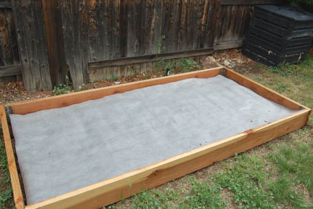 Weed-proof fabric barrier laid on top of dirt in the raised garden.