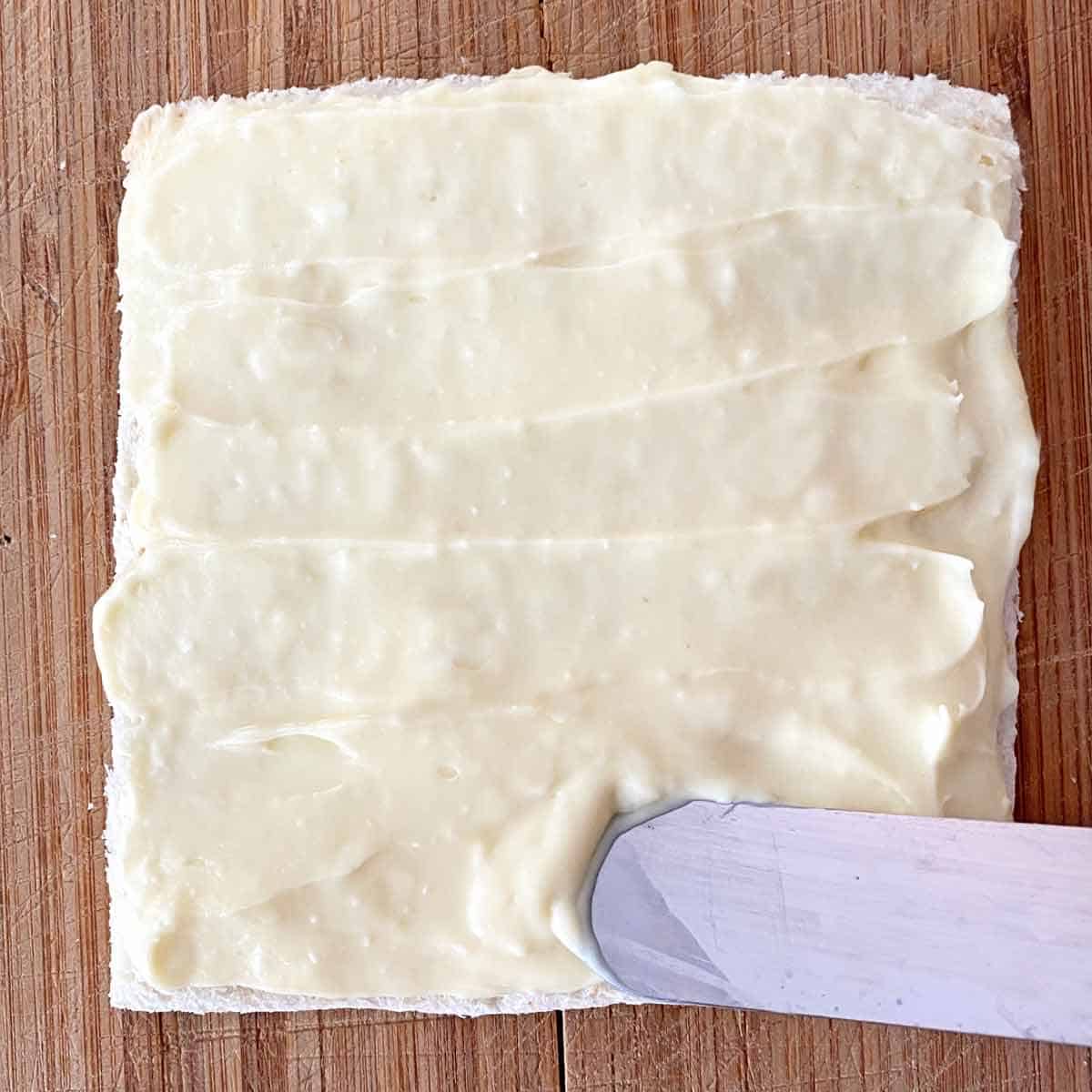 Spreading the trimmed bread slice with the sweetened cream cheese mixture.