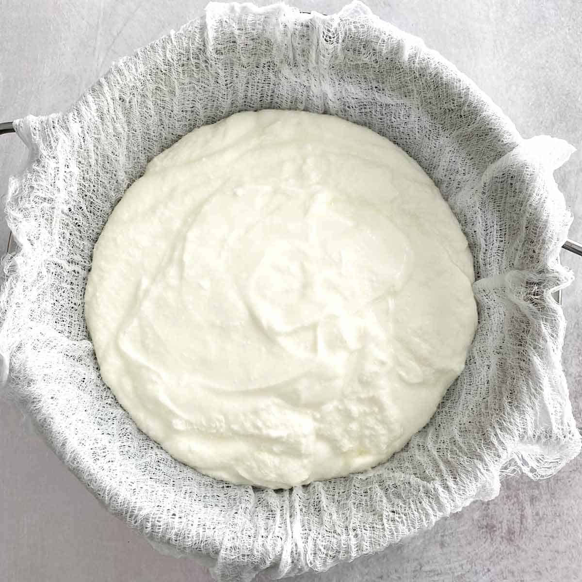 Greek yogurt in a strainer lined with cheesecloth.