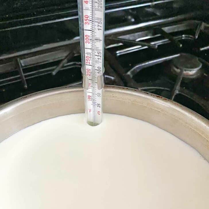 Milk in a saucepan with a candy thermometer.