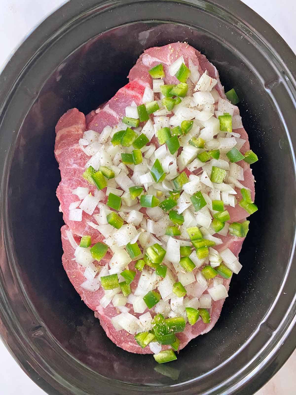 Uncooked ingredients for Mexican Carnitas in a black slow cooker Crock Pot.