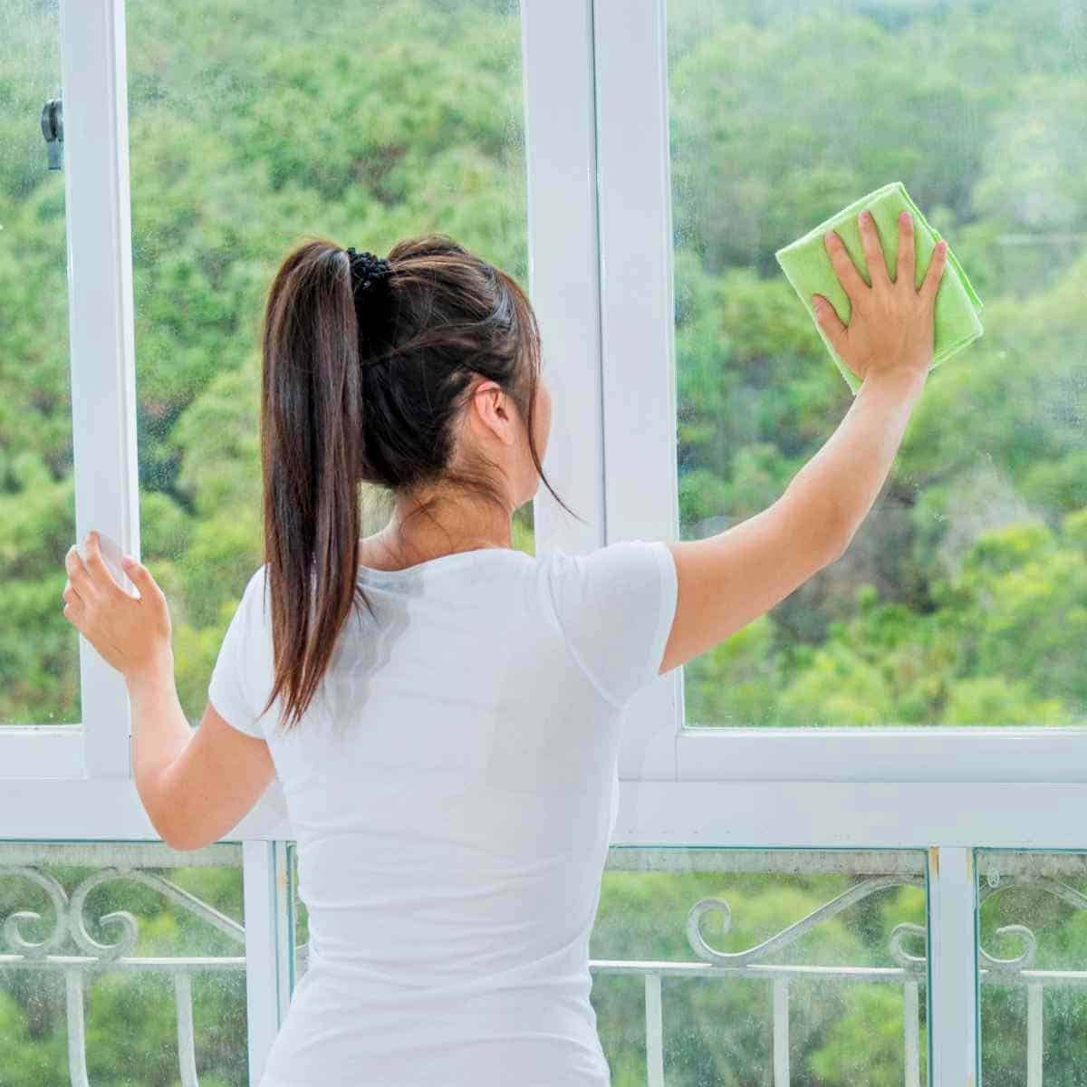 A woman cleaning a window with DIY vinegar window cleaner.