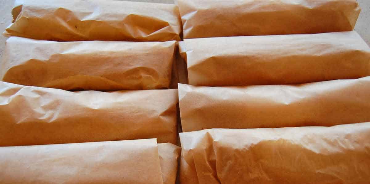 Eight prepared breakfast burritos wrapped in parchment paper.